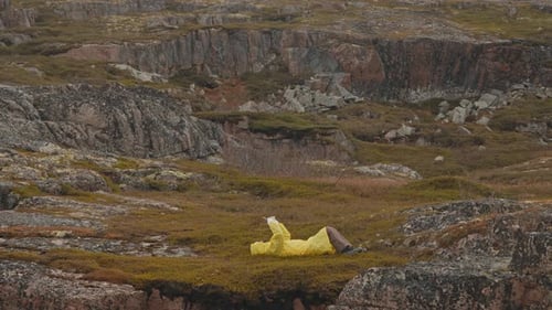 Person in Yellow Raincoat Lying in Rocky Wilderness