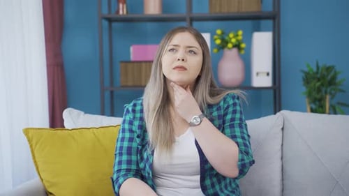 Woman Touching Sore Throat While Sitting On Couch