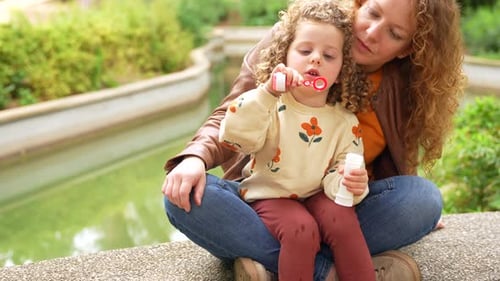 Playful Girl Blowing Bubbles in the Park with Her Mother