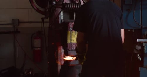 Professional blacksmith presses hot metal with machine in blacksmith workshop