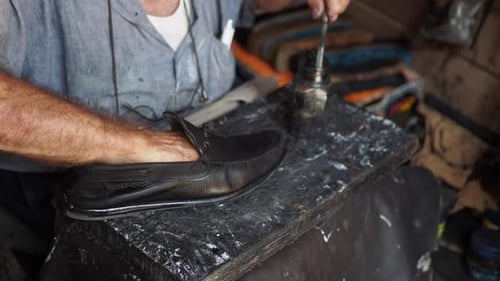 Les mains d'un cordonnier réparent les coutures de chaussures à l'aide d'une aiguille