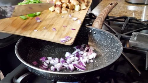 Pushing red onions and peppers into hot pan to cook, potatoes on wooden cutting board