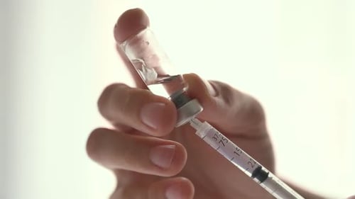 Nurse filling a syringe with vaccine dose on a white background