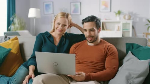Casal feliz e adorável se senta em um sofá em casa, o namorado segura, navega na Internet, faz e-sho