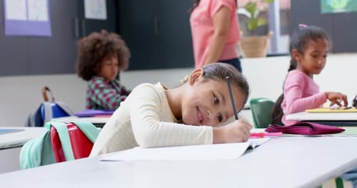 In school, girl smiling while writing in notebook at classroom desk