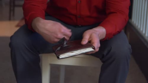 A white man's hands untie the binds of a leather bound journal or notebook and opens it.