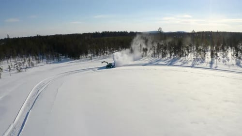 Aerial view orbiting snow covered forested wilderness tractor blower moving snowdrift across wintry