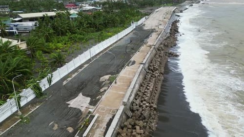 Aerial orbit of rough, murky waters crashing against coastal island boulevard road during stormy wea