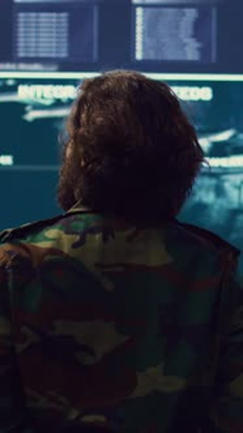 Man in Camo Uniform Stands Before Monitors