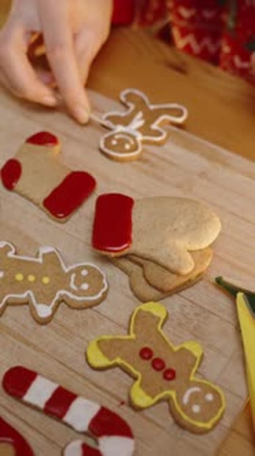 Vertical video. A Woman in a Festive Red Sweater Carefully Adds White Icing to a Gingerbread Man Coo