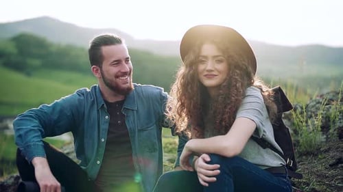 Young couple backpacking on holiday resting on a hill at sunset in nature