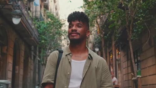Close up, young smiling man walks along the narrow street of the old city and looks around