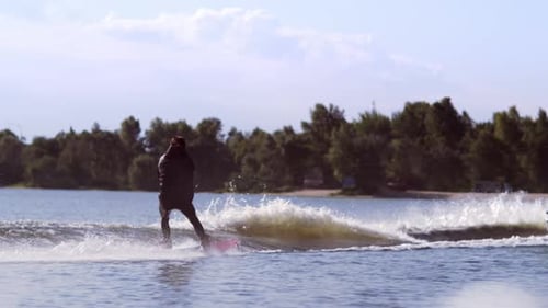 Wakeboarder carving across azure lake water behind motorboat on summer holiday