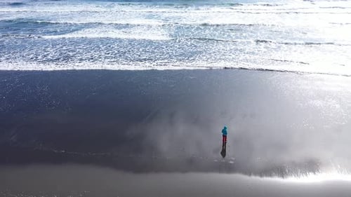 Aerial slow motion view of a female traveler relaxing on Atlantic ocean coast. Sea waves washing bl