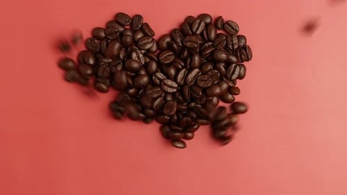Heart made from Roasted Coffee beans blowing out on pink top view