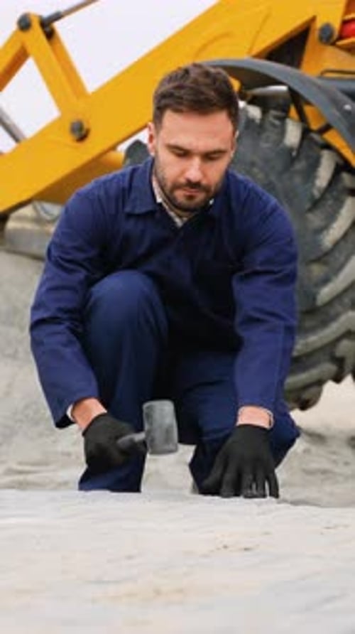 Construction Worker Leveling Pavement Near Heavy Machinery