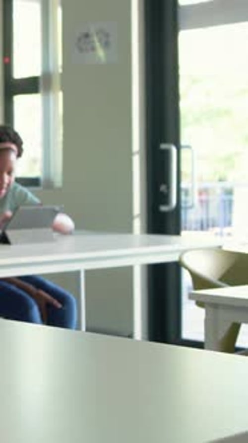 Vertical video: Tapping girl with pink headband using tablet at school desk, peer joining teamwork