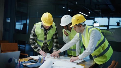 Three Engineers Discuss Blueprints and Plans in an Office Setting While Wearing Safety Helmets and