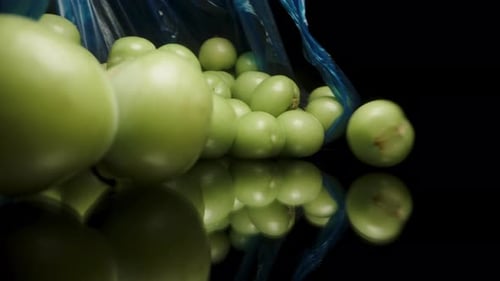 Las ciruelas verdes se derraman de una bolsa azul sobre una mesa negra. Primer plano en cámara lenta
.