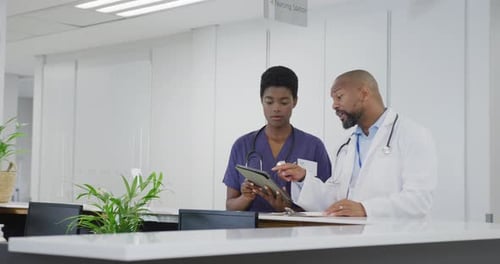 African american male and female doctors using tablet, talking at hospital