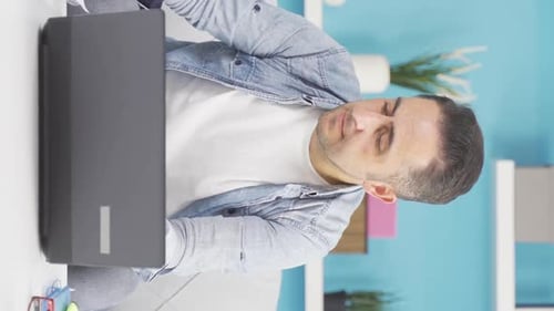 Vertical video of Man working on laptop throws files angrily.