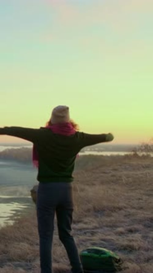 Individual with Raised Arms Celebrating Sunset View Over Serene Landscape with Open Sky