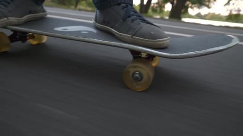 Skateboarding down a large hill in the park. Camera swings across the front of the board a few times
