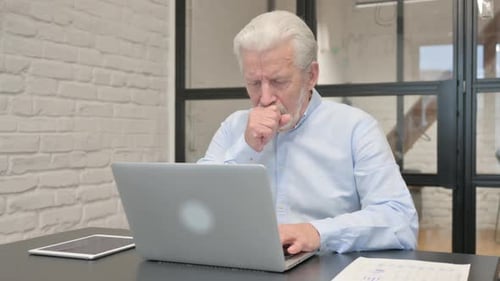 Coughing Senior Businessman Using Laptop in Office