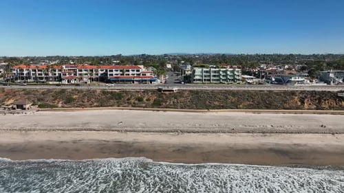 Aerial backward moving shot over the pacific ocean with the view of the sandy beach and the town of