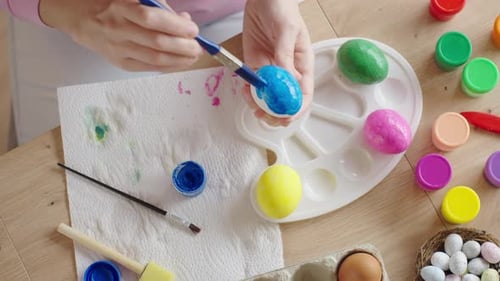 Woman painting Easter egg at home with pastel paints