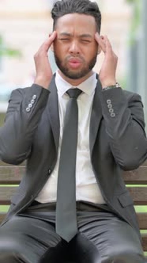 Man in Suit Massaging Temples on Bench Outdoors
