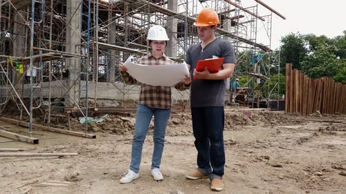Construction manager and engineer discussing and checking plans on construction site.
