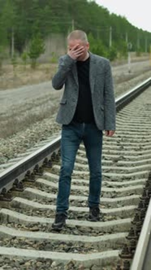 Contemplative Man in Grey Suit Walking Along Railway Tracks in Forest