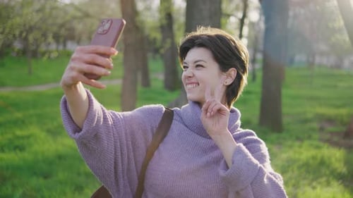 Woman Takes Selfie in a Green Park During Daylight While Enjoying the Outdoors and Interacting with