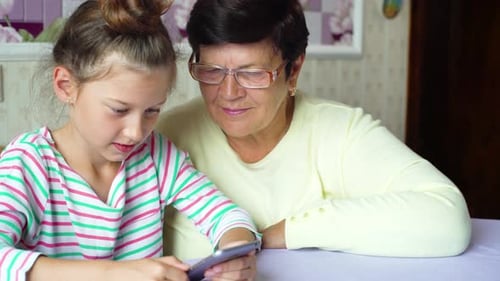 Girl and Grandmother Using Smartphone Together Indoors