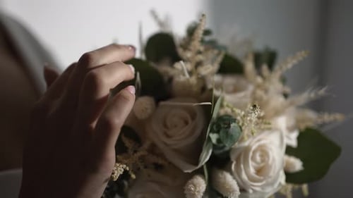 Close up of hands delicately holding a wedding bouquet, highlighting soft white roses.