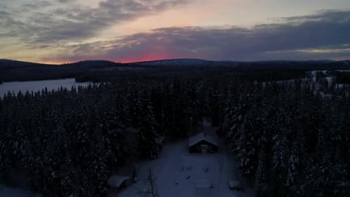 Aerial view towards secluded Lapland woodland cabin surrounded by snow covered wintry forest at dayb