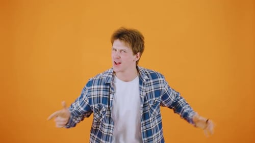 In a Studio with an Orange Backdrop a Man in a Plaid Shirt Poses Confidently Exuding Coolness and
