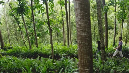 Young couple walk on path through green forest in Indonesia, side view