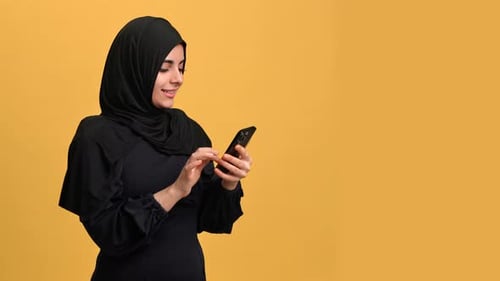 Contemporary Muslim Woman in Traditional Hijab Using Modern Smartphone Portrait in Orange Studio