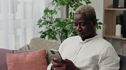 Young Adult Using Cellphone on Sofa Indoors