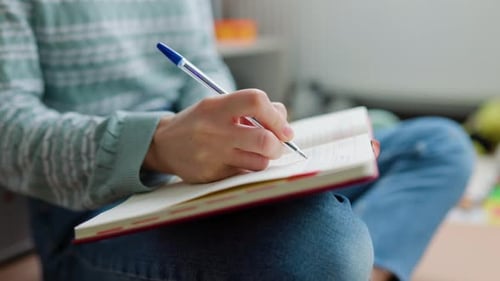 Side View Blurred Background Girl Sitting on Floor and Holding Notebook with Notes on Her Lap