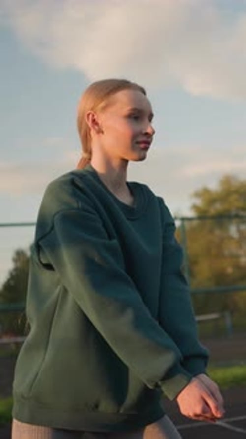 Young Woman Stretching Arms on Outdoor Basketball Court