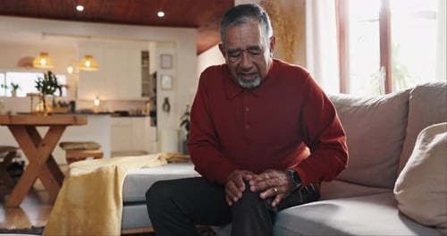 Relax, sofa and senior man with knee pain, injury or muscle sprain in living room at nursing home