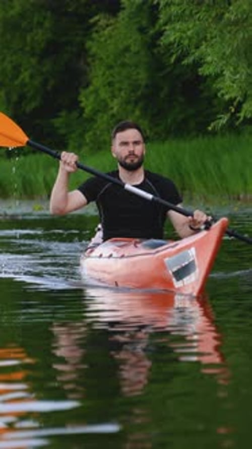 Kayaker Paddling in River or Lake with Lush Green Forest in Background