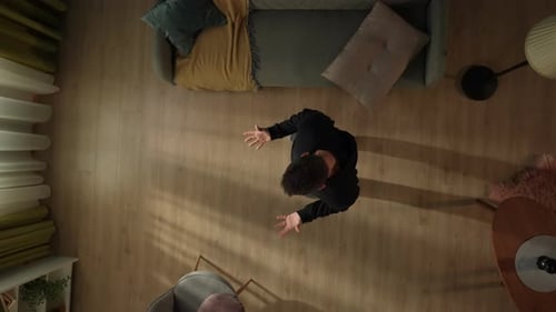 Top View of an Unhappy Man in the Living Room Who Has His Hands Up and is Screaming in Despair