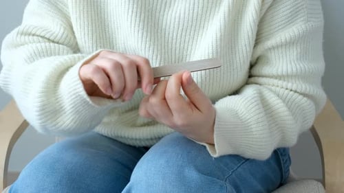 Eine Frau sitzt auf einem Stuhl und macht Maniküre mit einer Nagelfeile.