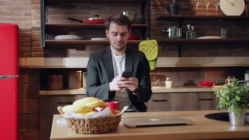 Man in kitchen looks at his cell phone