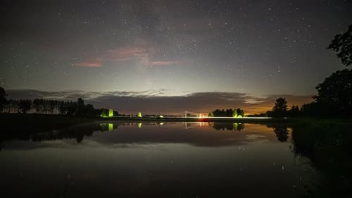 Zeitrafferaufnahme von Sternen, die kurz vor Sonnenaufgang über einer Straße neben einem See in ländlicher Landschaft sichtbar sind.