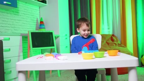 Excited Child Playing with Colorful Plasticine at Table